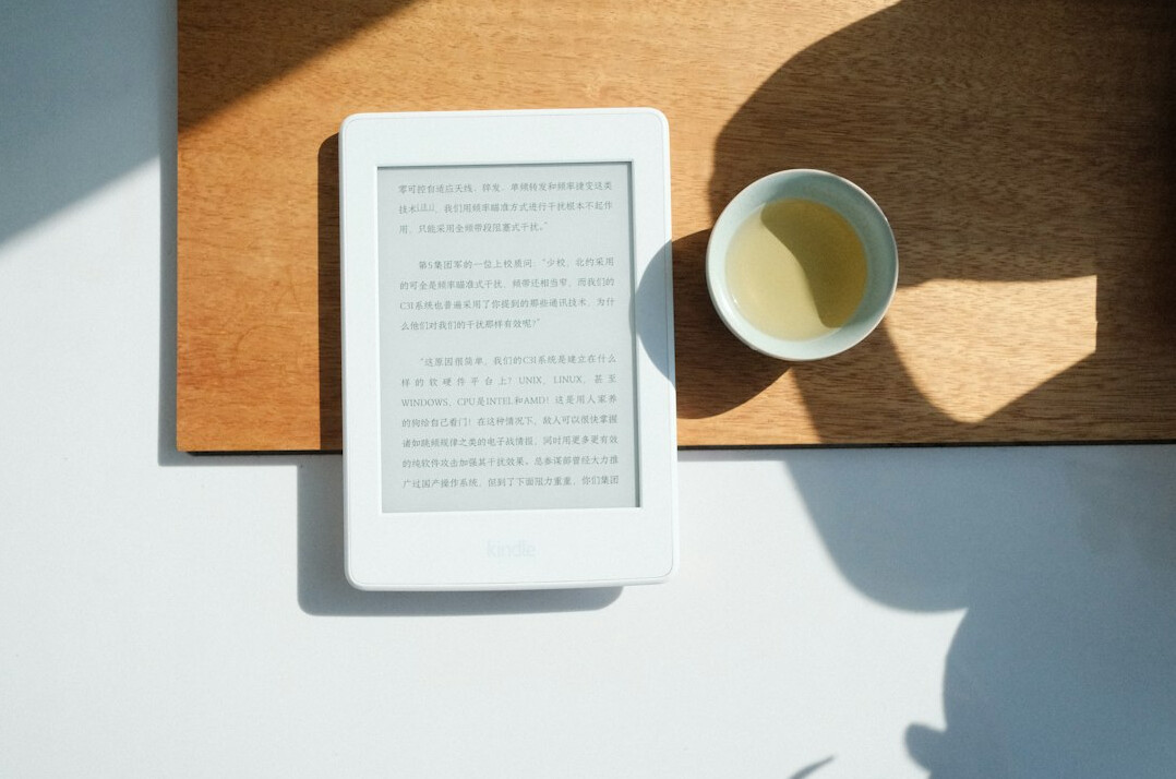 Tablet and reading glasses on a bright wooden table with a cup of tea
